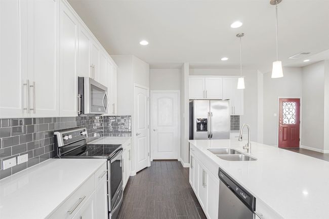 Kitchen featuring appliances with stainless steel finishes, dark wood-type flooring, tasteful backsplash, light countertops, and recessed lighting | Image 11