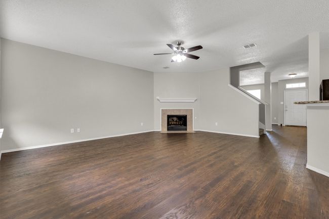 Unfurnished living room with ceiling fan, a fireplace, dark wood-style floors, baseboards, and a textured ceiling | Image 9
