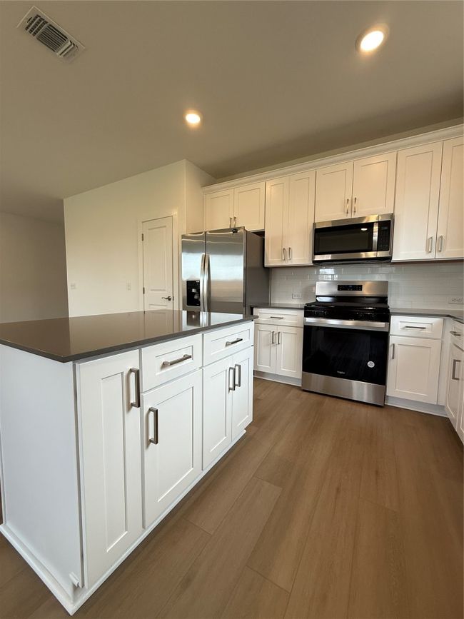Kitchen with stove, freestanding refrigerator, dark countertops, white cabinets, and dark wood-type flooring | Image 19