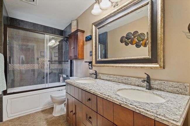 Full bathroom featuring toilet, double vanity, shower / bath combination with glass door, and tile patterned floors | Image 26