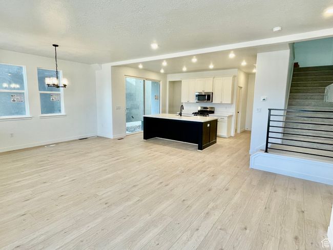 Kitchen featuring stainless steel appliances, an island with sink, a chandelier, light countertops, and open floor plan | Image 5
