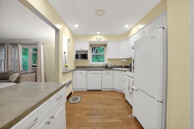 Kitchen with white appliances, light wood finished floors, white cabinets, a textured ceiling, and open floor plan | Image 11