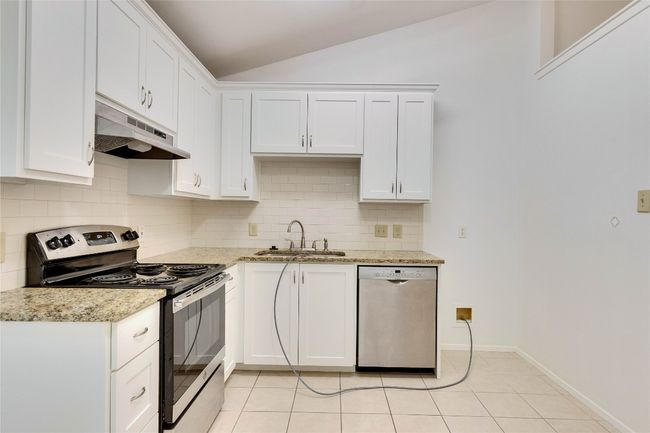 Kitchen with stainless steel appliances, lofted ceiling, backsplash, white cabinetry, and under cabinet range hood | Image 11