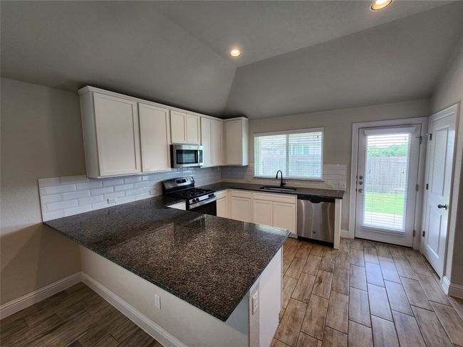 Kitchen with appliances with stainless steel finishes, a peninsula, white cabinetry, tasteful backsplash, and light wood-style flooring | Image 6
