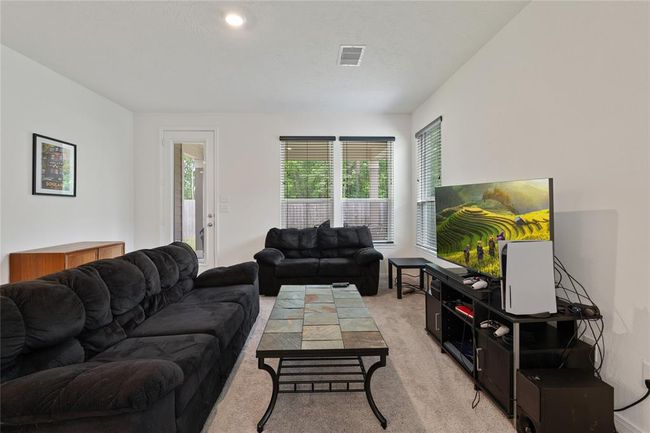 Bright living room with cozy seating, large windows, and a modern entertainment setup. Neutral walls and carpet create a warm, inviting atmosphere. Ideal for relaxation and entertaining. | Image 9