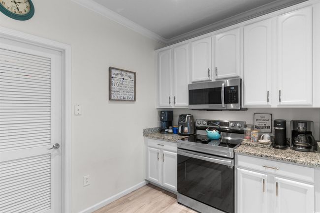 Kitchen featuring stainless steel appliances, light wood finished floors, crown molding, baseboards, and white cabinets | Image 5
