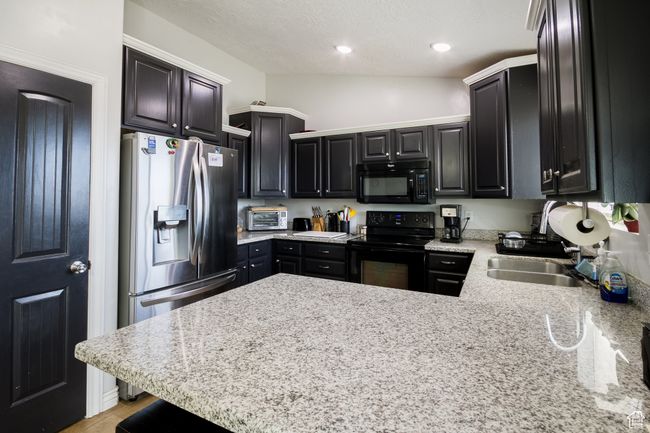Kitchen featuring a peninsula, a sink, recessed lighting, dark cabinets, and black appliances | Image 9