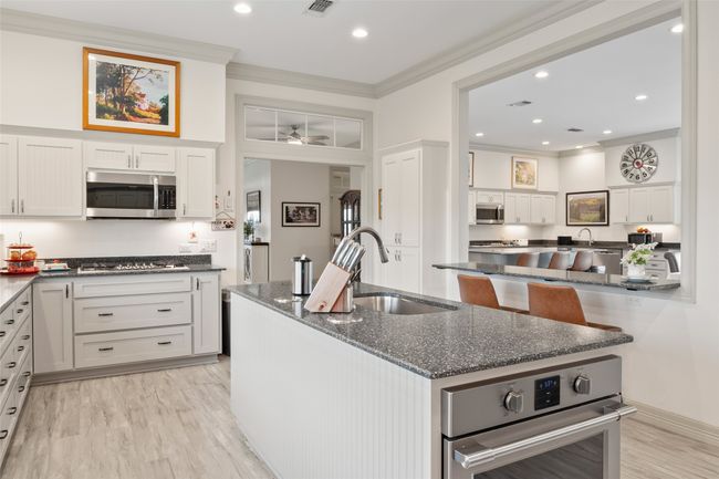 Kitchen featuring a center island with sink, dark stone counters, appliances with stainless steel finishes, white cabinetry, and a sink | Image 14