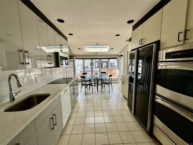Kitchen featuring backsplash, a sink, light tile patterned flooring, a skylight, and appliances with stainless steel finishes | Image 4