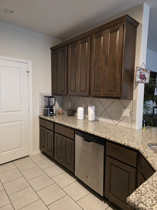 Kitchen with dishwasher, light tile patterned flooring, dark brown cabinets, decorative backsplash, and light stone counters | Image 4