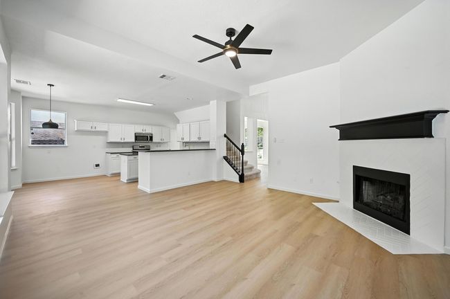 Unfurnished living room featuring a ceiling fan, light wood-style floors, a fireplace with flush hearth, and healthy amount of natural light | Image 9