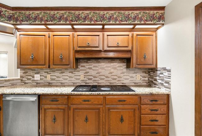 Kitchen featuring black electric cooktop, stainless steel dishwasher, backsplash, and brown cabinetry | Image 11