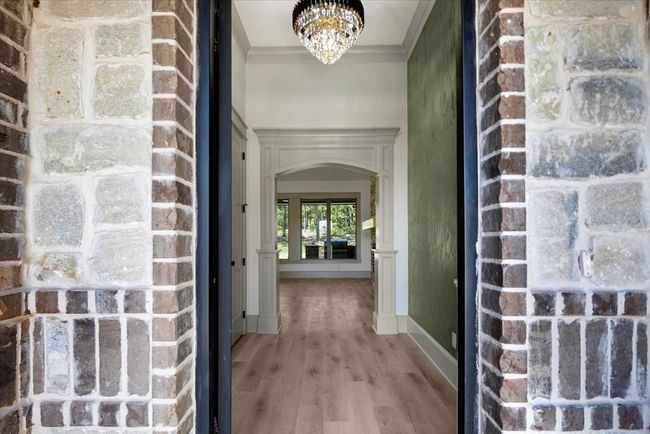 Corridor with crown molding, light wood-type flooring, arched walkways, and a chandelier | Image 40