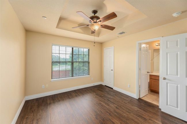 Unfurnished bedroom featuring a tray ceiling, dark wood finished floors, ensuite bathroom, and a ceiling fan | Image 20