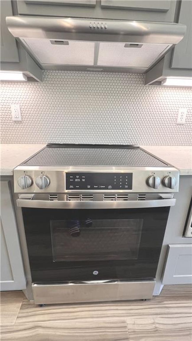Kitchen view of extractor fan, stainless steel electric stove, tasteful backsplash, and wood finished floors | Image 22