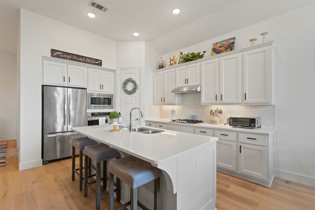 Kitchen featuring stainless steel appliances, decorative backsplash, a kitchen breakfast bar, under cabinet range hood, and recessed lighting | Image 24