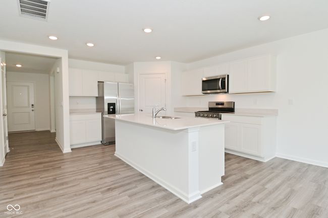 kitchen featuring stainless steel appliances, luxury vinyl plank flooring, Large island with sink, white cabinetry, and quartz countertops | Image 8