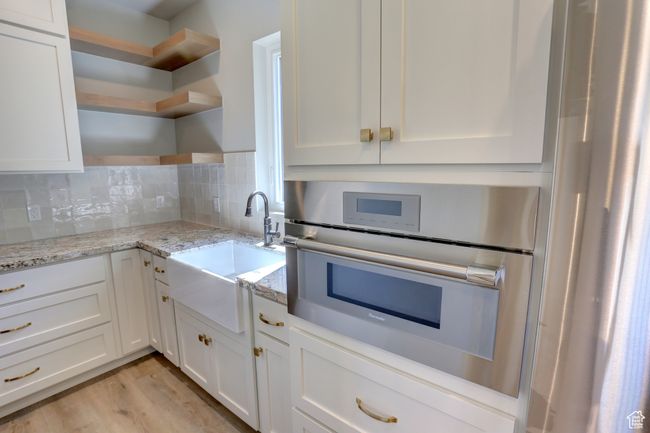 Kitchen with open shelves, stainless steel oven, white cabinets, and decorative backsplash | Image 13