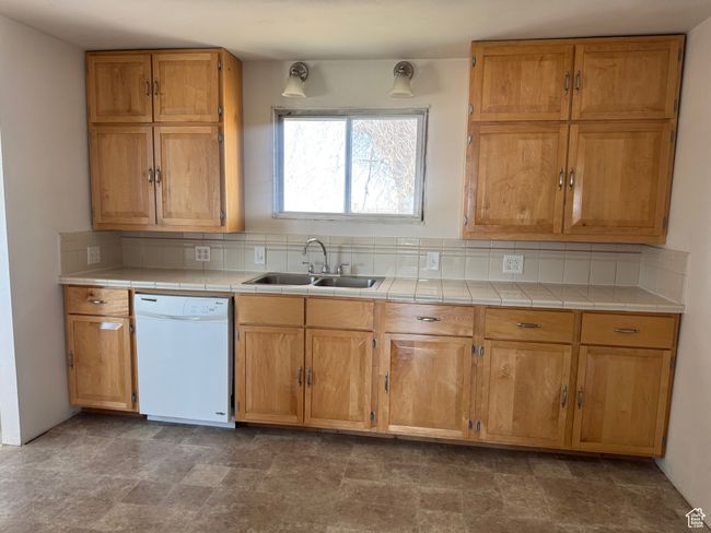 Kitchen with tile counters, tasteful backsplash, white dishwasher, and a sink | Image 19