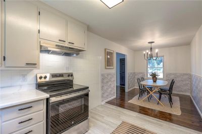 Kitchen with an inviting chandelier, light hardwood / wood-style flooring, electric range, pendant lighting, and tasteful backsplash | Image 2