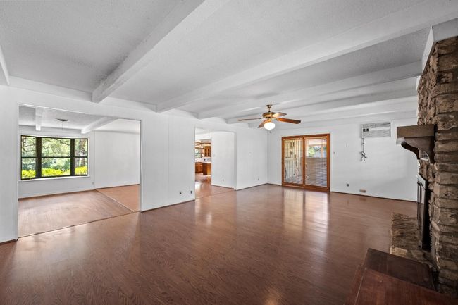 Unfurnished living room featuring wood finished floors, beamed ceiling, a ceiling fan, and healthy amount of natural light | Image 8