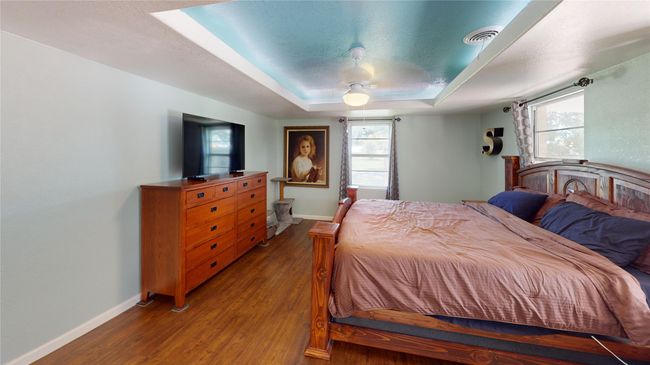 Bedroom with dark wood-style flooring, a tray ceiling, ceiling fan, and a textured ceiling | Image 18
