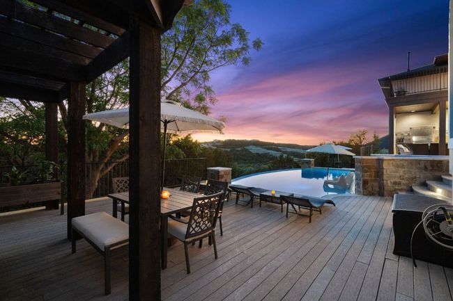 Deck at dusk with outdoor dining area, a pergola, and an infinity pool | Image 7