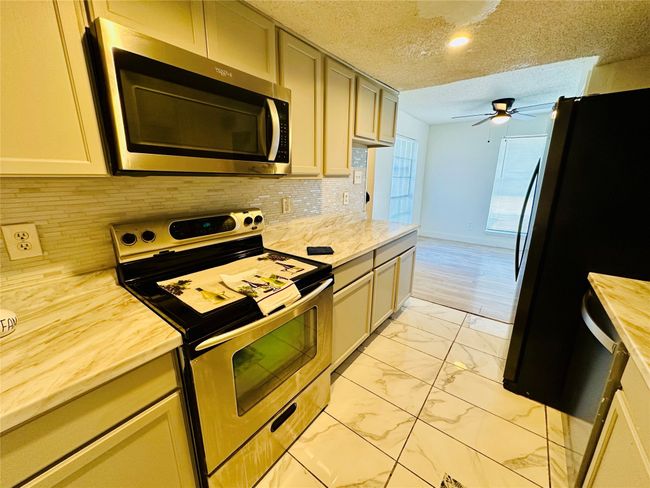 Kitchen featuring appliances with stainless steel finishes, light marble finish floors, ceiling fan, tasteful backsplash, and a textured ceiling | Image 5