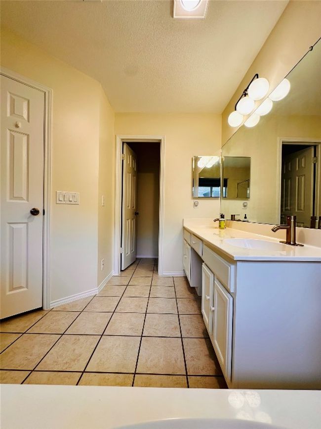 Bathroom with a textured ceiling, a sink, tile patterned floors, double vanity, and baseboards | Image 22