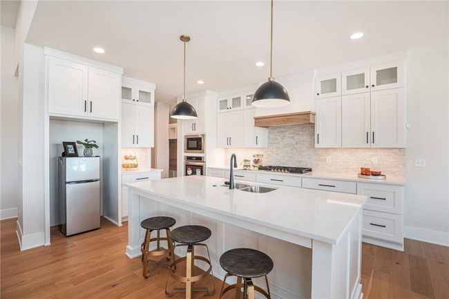 Kitchen featuring stainless steel appliances, decorative backsplash, light wood finished floors, light countertops, and white cabinets | Image 9