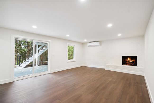 Unfurnished living room with a wall mounted air conditioner, dark wood-style flooring, a fireplace, stairs, and recessed lighting | Image 29