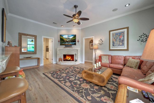 Living room featuring a warm lit fireplace, a ceiling fan, visible vents, ornamental molding, and wood finished floors | Image 13