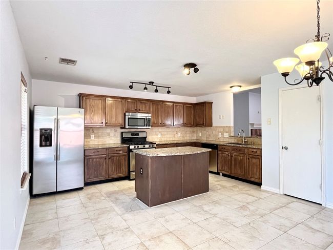 Kitchen featuring stainless steel appliances, tasteful backsplash, a chandelier, a center island, and light stone countertops | Image 7