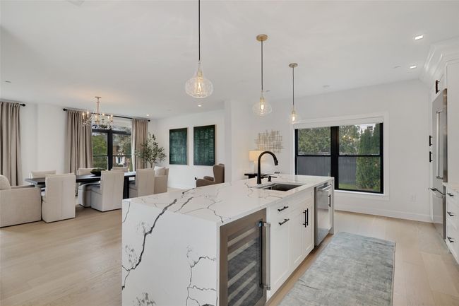 Kitchen featuring beverage cooler, light wood finished floors, stainless steel dishwasher, a sink, and white cabinetry | Image 7