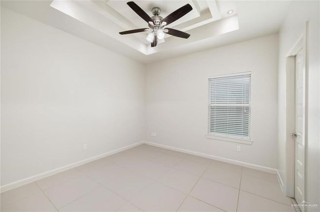Empty room with a tray ceiling, baseboards, ceiling fan, and light tile patterned floors | Image 5