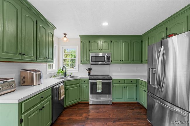 Kitchen featuring a sink, appliances with stainless steel finishes, light countertops, backsplash, and dark wood-style flooring | Image 17