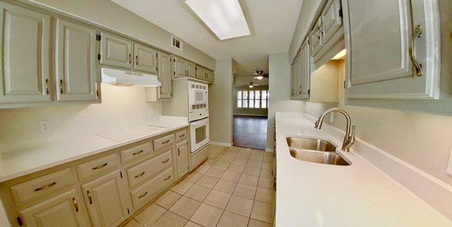 Kitchen featuring under cabinet range hood, light countertops, white appliances, light tile patterned floors, and a sink | Image 5