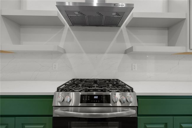 Kitchen with stainless steel range with gas cooktop, exhaust hood, green cabinets, and backsplash | Image 13