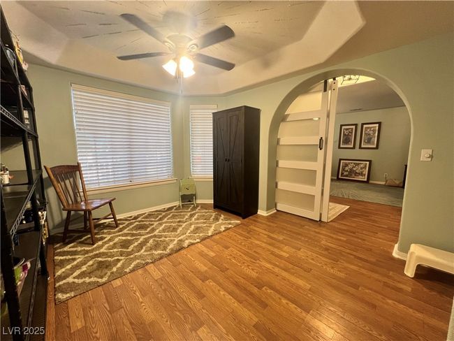 Unfurnished room featuring ceiling fan, arched walkways, wood finished floors, built in features, and a raised ceiling | Image 12