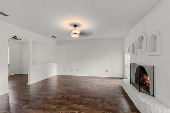 Unfurnished living room with hardwood / wood-style floors, a brick fireplace, a textured ceiling, baseboards, and ceiling fan | Image 6