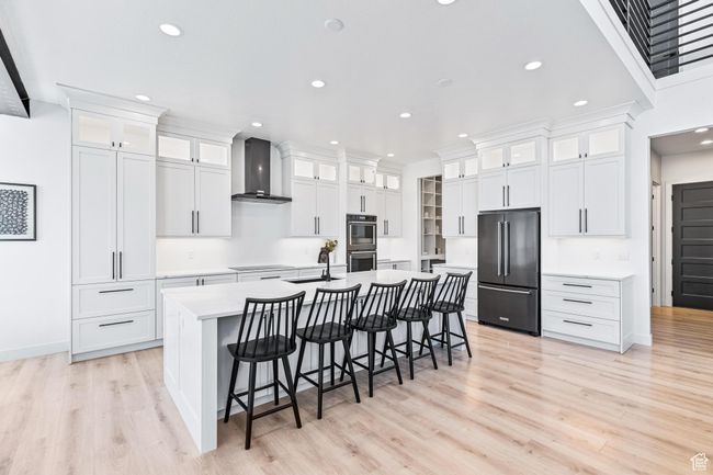Kitchen with light wood-style floors, a kitchen island with sink, wall chimney range hood, and black appliances | Image 54