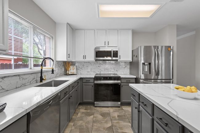 The kitchen is a true centerpiece with quartz countertops, stylish two-tone cabinetry, a deep stainless steel undermount sink, elegant backsplash, updated fixtures, stainless steel appliances. | Image 10