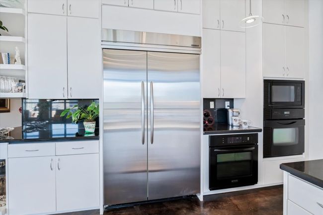 Kitchen with black appliances, open shelves, finished concrete flooring, Ink granite countertops, and white cabinetry | Image 8