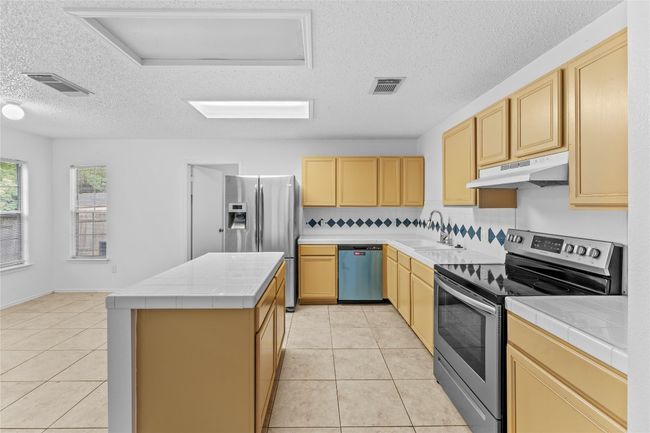 Kitchen with appliances with stainless steel finishes, under cabinet range hood, tile counters, a sink, and light tile patterned flooring | Image 12
