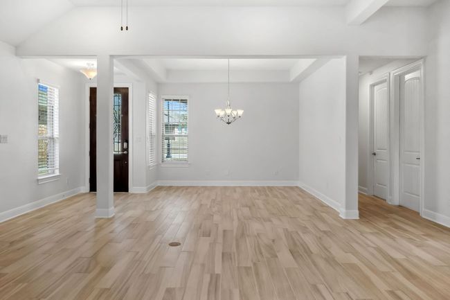 Unfurnished dining area with baseboards, light wood finished floors, an inviting chandelier, a tray ceiling, and vaulted ceiling | Image 9