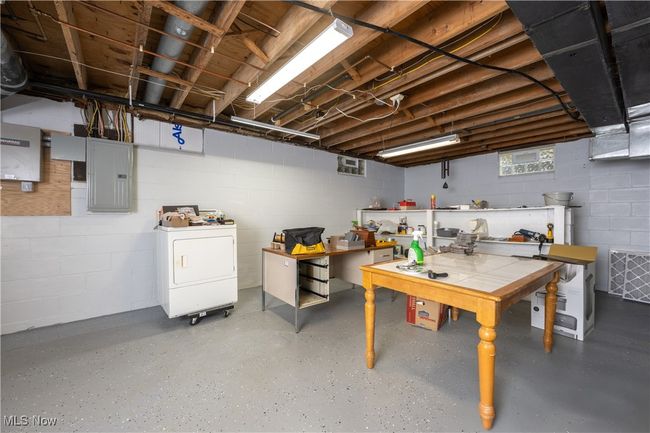 Below grade area featuring concrete block wall, electric panel, washer / dryer, and a workshop area | Image 33