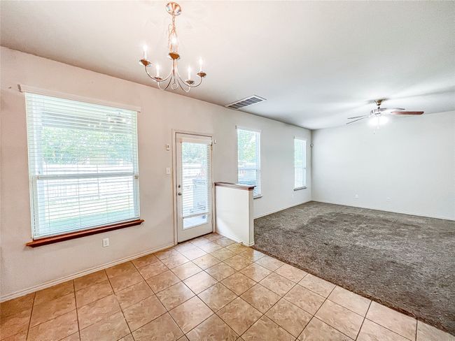 Empty room with a chandelier, light tile patterned flooring, light colored carpet, and a ceiling fan | Image 11