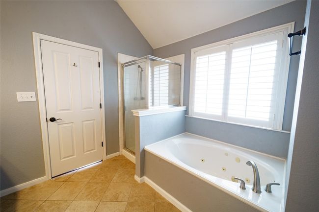 Bathroom with a stall shower, a tub with jets, lofted ceiling, tile patterned floors, and baseboards | Image 19