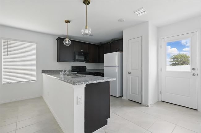 Kitchen with a sink, black appliances, light tile patterned flooring, a peninsula, and visible vents | Image 5
