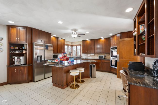kitchen featuring light tile patterned floors, a breakfast bar, open shelves, appliances with stainless steel finishes, and a center island | Image 14